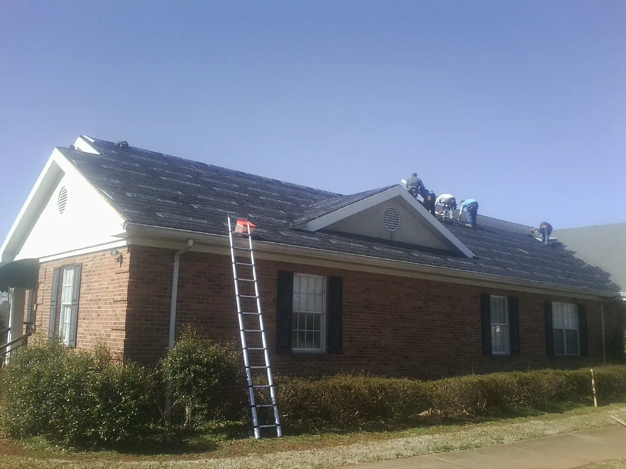 Crew tearing shingles off a brick ranch roof with a ladder set — Metal Roof Repair work by our crew in Adelphi