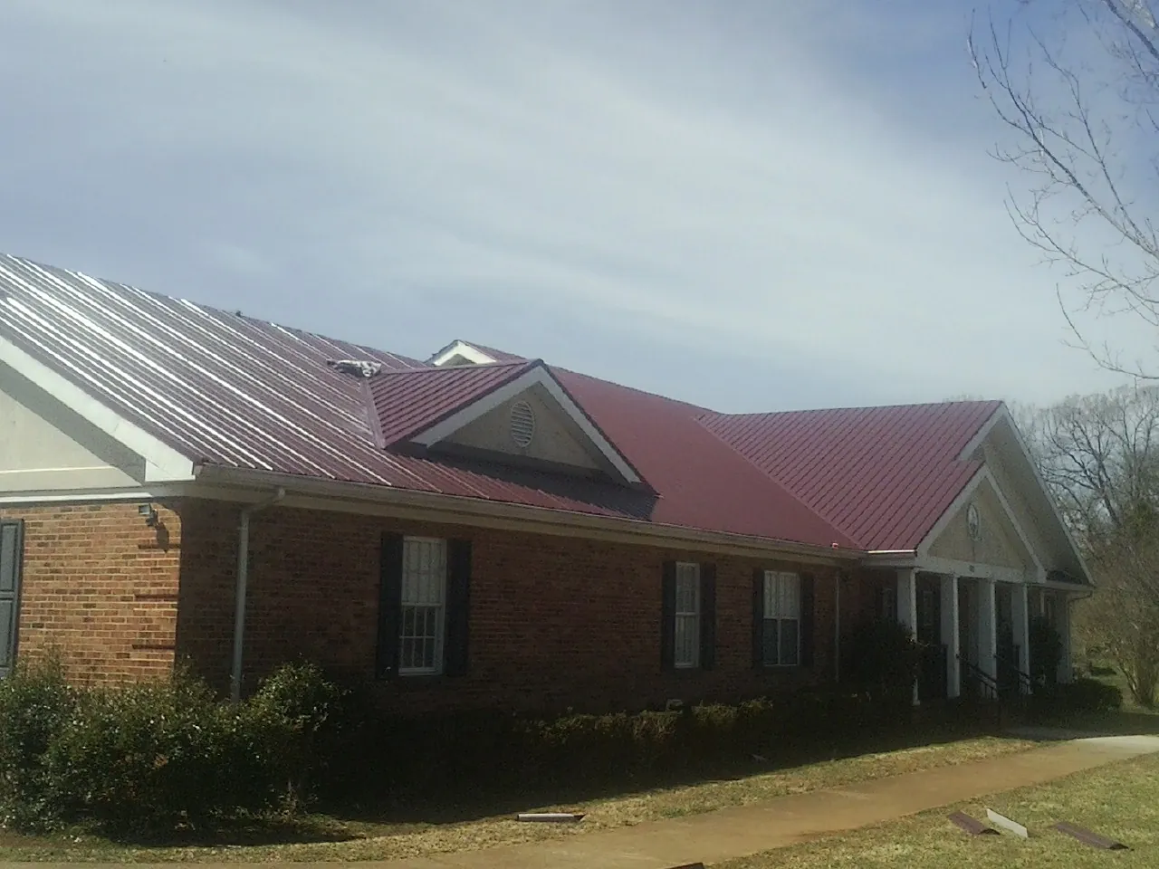 Red metal roof with gabled entries on a long brick building, from a Hail Damage Roof Repair job in Adelphi