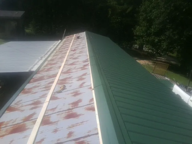 Old rusted panels beside newly installed green metal roofing — Wind Damage Roof Repair by Roofing Brothers in Adelphi