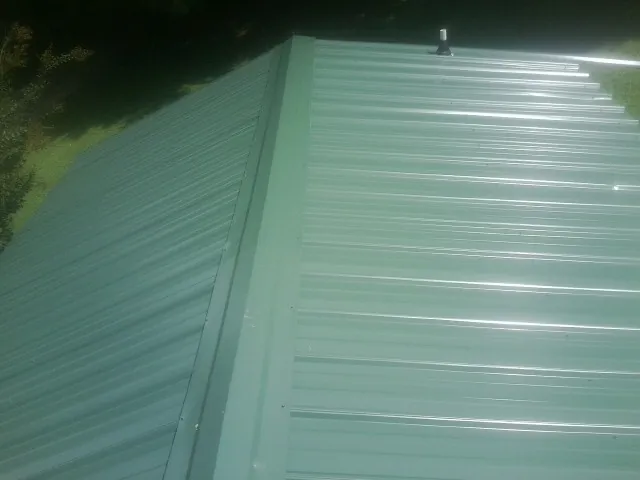New green metal panels meeting at the ridge of a roof — Flat Roof Repair work by our crew in Adelphi