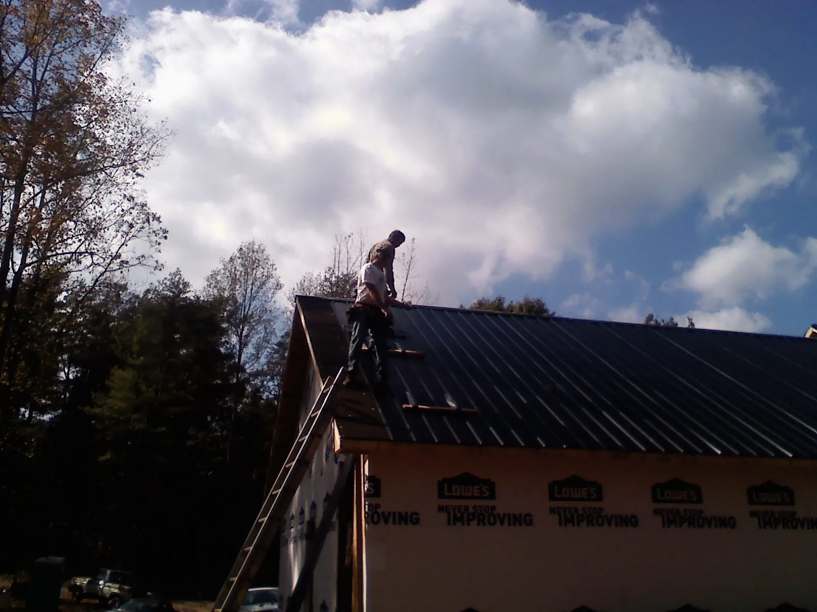 Roofer fastening dark metal panels high against a cloudy sky, from a Roof Inspection job in Adelphi